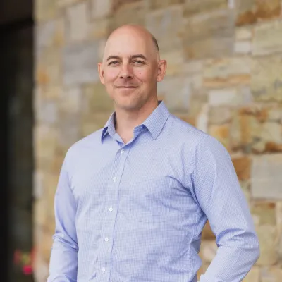 Eric smiles at the camera in a headshot. He is wearing a light blue button-down shirt.