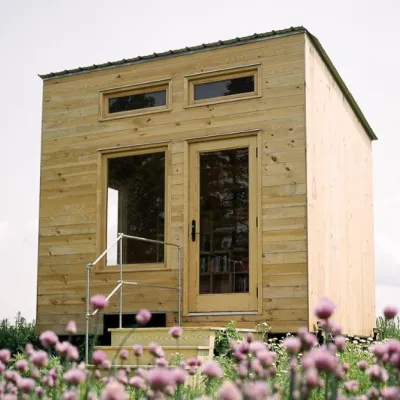 A finished tiny library stands in a field with sky in the background and red clover in the foreground.
