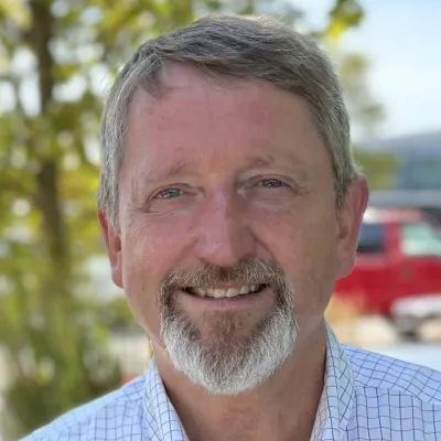 Gunnar smiles at the camera. He is wearing a white button down shirt. He has blue eyes and a goatee. 