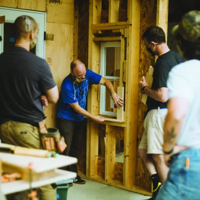A person demonstrates on a trimmed window opening inside a framed structure.