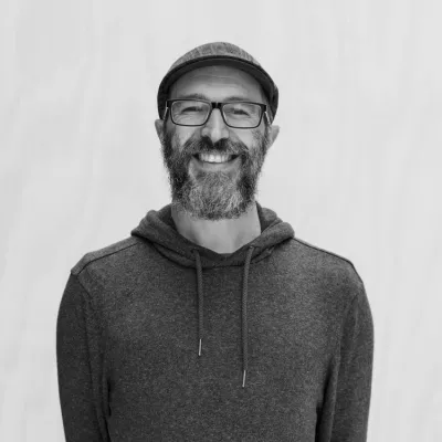 Jacob smiles at the camera in a black and white headshot. He is wearing a cap and hooded sweatshirt.