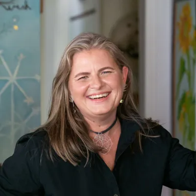 Janine smiles at the camera. Her blonde hair down and she is wearing a black button-down shirt.