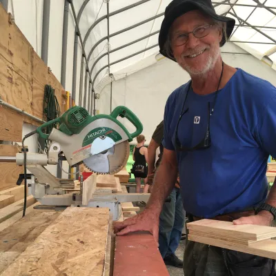 Jim smiles at the camera in an outdoor classroom. He is wearing a brimmed hat and blue t-shirt.