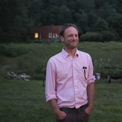 Joel smiles outside at dusk. He is looking to the right of the camera, has short blond hair and is wearing a pink button-down shirt. 