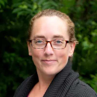 Katelyn smiles at the camera in a headshot. Her brown hair is pulled back and she is wearing glasses, a pink shirt and black sweater.