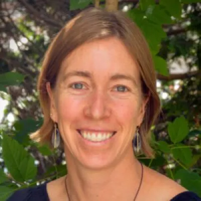 Laura smiles in a headshot outside in front of trees. She has short, blonde hair and light eyes.