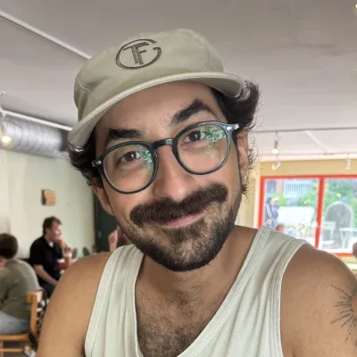 Leo smiles at the camera. He has dark hair, a beard and glasses.