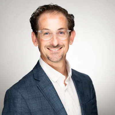 Matt smiles at the camera in a headshot with short curly brown hair and a blue blazer.