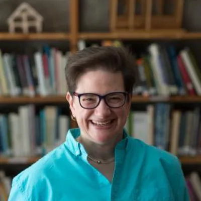 Michelle Lee smiles in front of bookshelves. She has short brown hair, glasses, and a turquoise collared shirt.