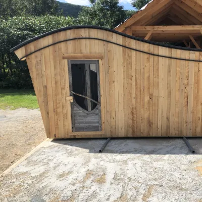 A shed with a curved roof and vertical siding is photographed outside on a sunny day.