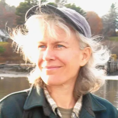 Sarah is photographed outside in the sun, looking up and to the left. She is wearing a cap and jacket.