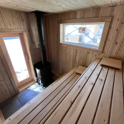The interior of a sauna with 3 tiers of seating and a woodstove. 