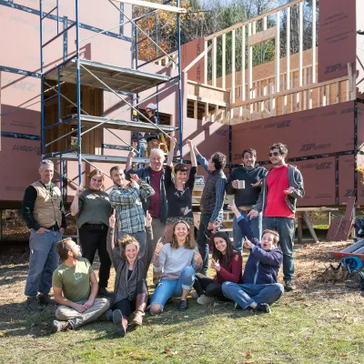A group of people smile at the camera in front of a partially framed bunkhouse.