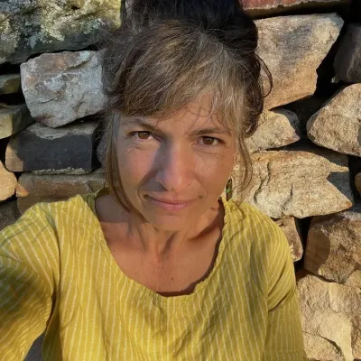 Thea looks at the camera, outside in front of a rock wall. She is wearing a yellow shirt.