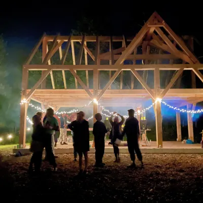 Night time shot of silhouetted people around a raised timber frame. There are lights strung up in and around the frame.