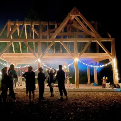 A timber frame at night with lights strung up and party goers silhouetted in the foreground.