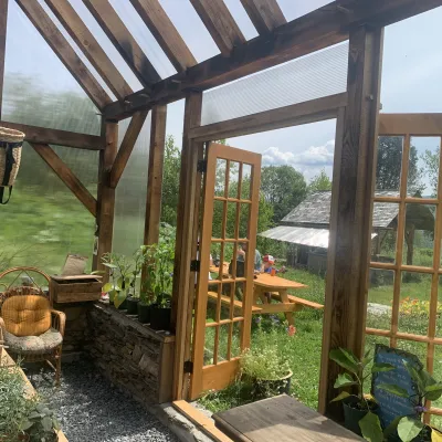 Interior shot of a timber frame greenhouse. Farm is visible outside of the clear walls and roof, and there are plants inside.