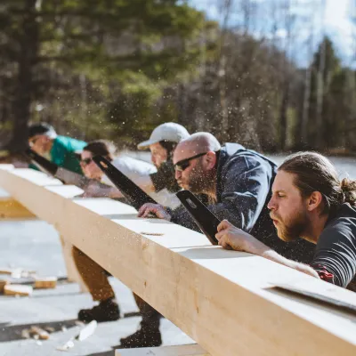 Several students lined up along a timber blow sawdust as they make cuts with hand saws.