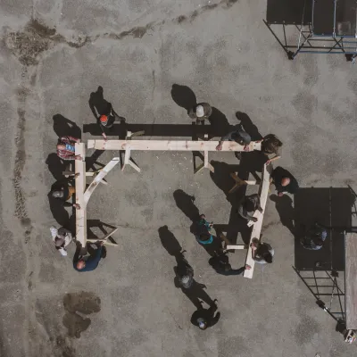 Aerial view of a timber frame bent being raised on a blacktop.