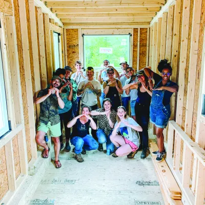 A group picture of students inside a framed tiny house, smiling at the camera.