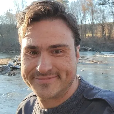 Man smiles for a selfie in front of a river