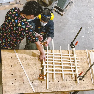 Two people shot from above weave strips of plywood 