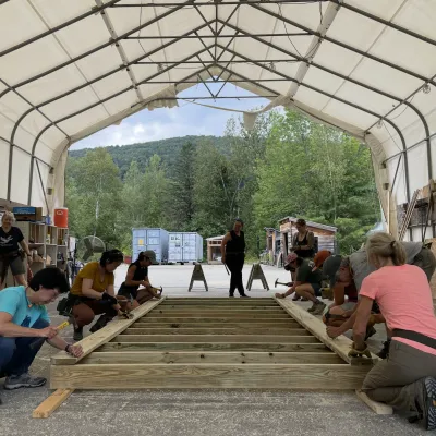 A group of students builds a floor system in an outdoor classroom.