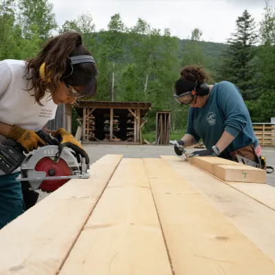 Shot of two carpentry students: one making a cut with a circular saw and one marking a piece of lumber.