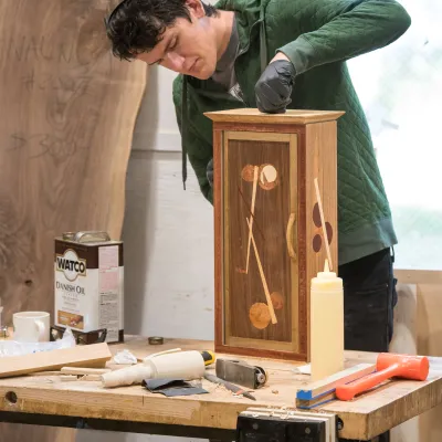 a young man applies stain to a wooden box they have made