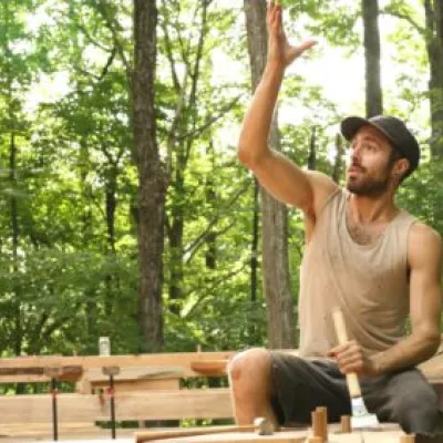 Man in a hat sitting on a timber frame in the forest