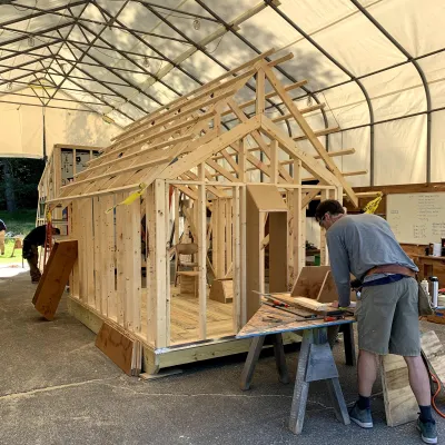 A student with their back to the camera is photographed in front of a framed cabin with pop out windows