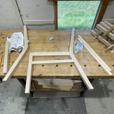 A glued-up portion of a chair lies on a work table in a woodshop