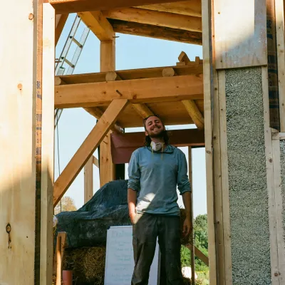 A student smiles from inside a framed building with hempcrete walls.
