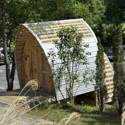 A structure with a gothic arch shaped roof surrounded by trees and bushes.