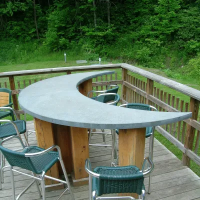 Photo of a crescent moon-shaped concrete countertop with bar stools outside on a deck.