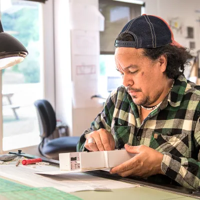 A student sitting at a drafting table and building an architectural model. 