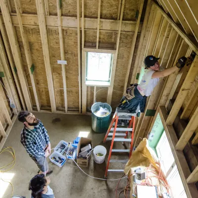 Several people photographed from above rough in wiring in a framed building.
