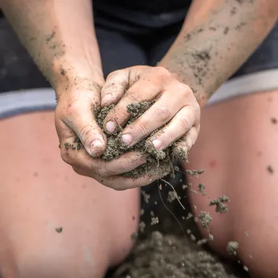 A person wearing shorts and kneeling with a close up on their hands holding earthen material.