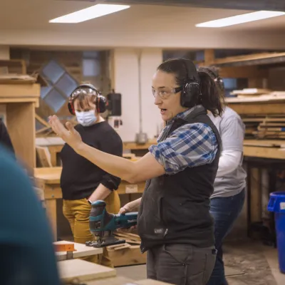 An instructor gestures in the woodshop in front of a group of students