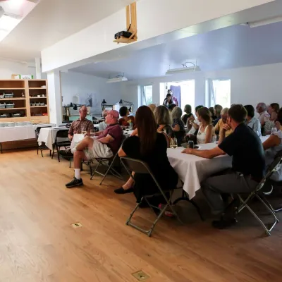Shot of an event in the main studio, with people sitting at long tables set up for a meal.