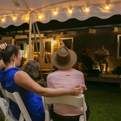 Two people shot from behind watch music under a white tent at night.