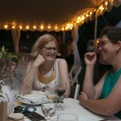 Two guests converse at a table under a white tent with string lights at night.