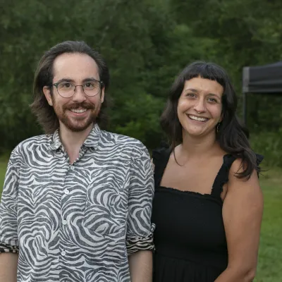 Two people smile at the camera, outside on a lawn.