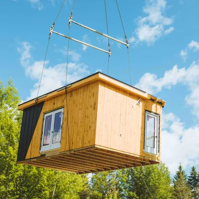 A building is craned through the air with blue sky and trees in the background.