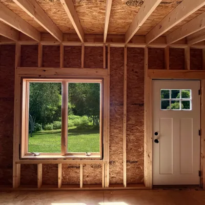 The interior of a wood framed cabin looking on a green lawn. 