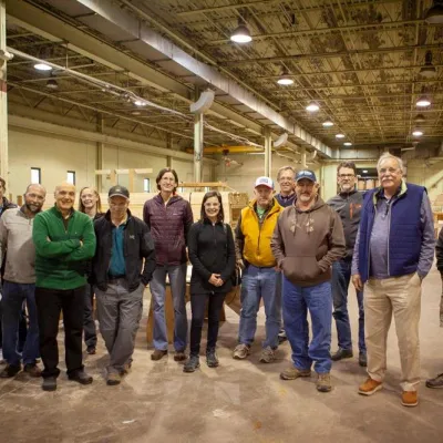 A group of 15 students and instructors inside a factory building looking at the camera and smiling. 