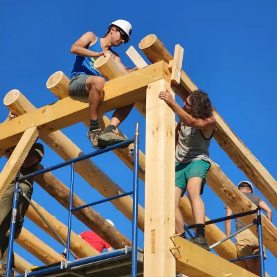 Two students installing round pole rafters on a timber frame structure.