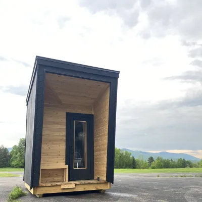 A small, modern wooden sauna with a black-trimmed door and angled roofline.