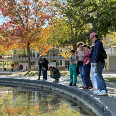 A group of students stand looking into a reflecting pool with fall foliage in the background