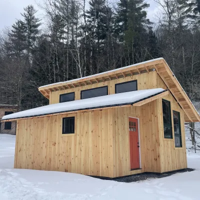 Casa Virga, a small house with vertical siding, a clerestory, and red door photographed in the snow.